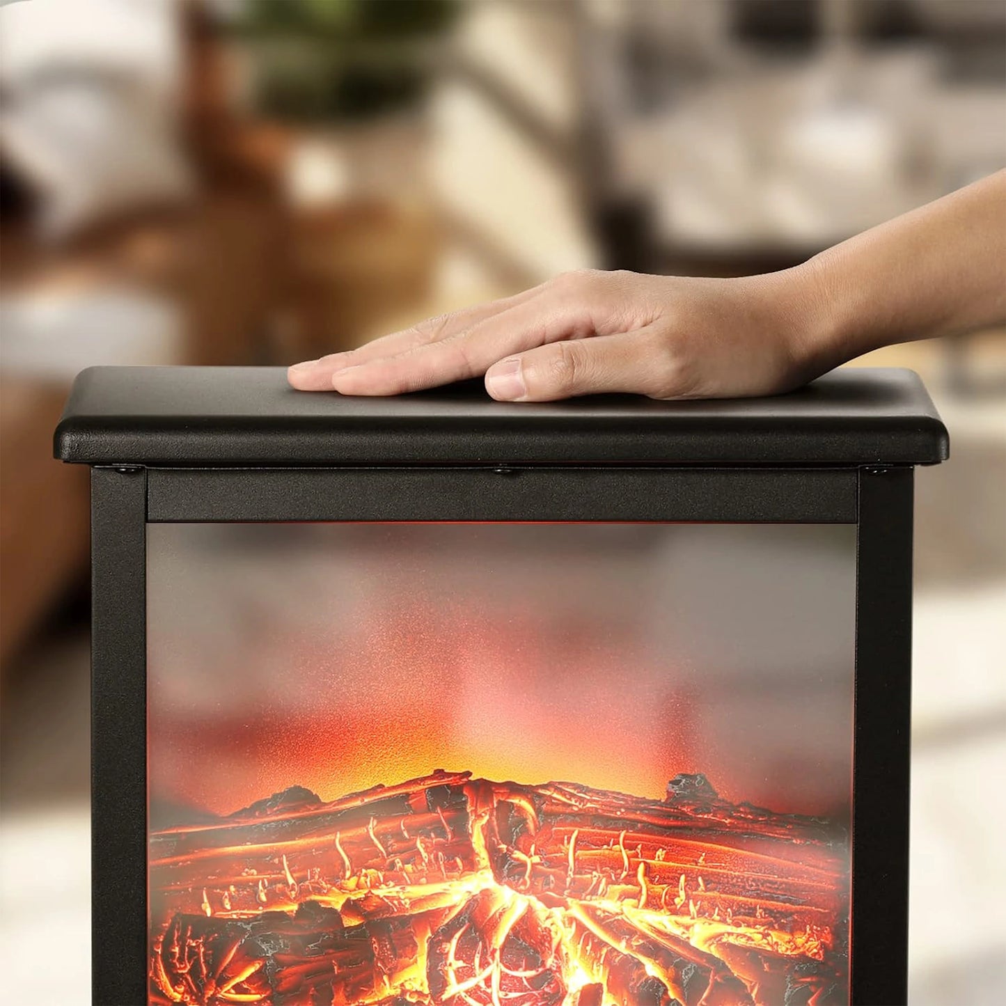 Hand resting on a black box with a fiery design, resembling a fireplace, against a blurred indoor background.