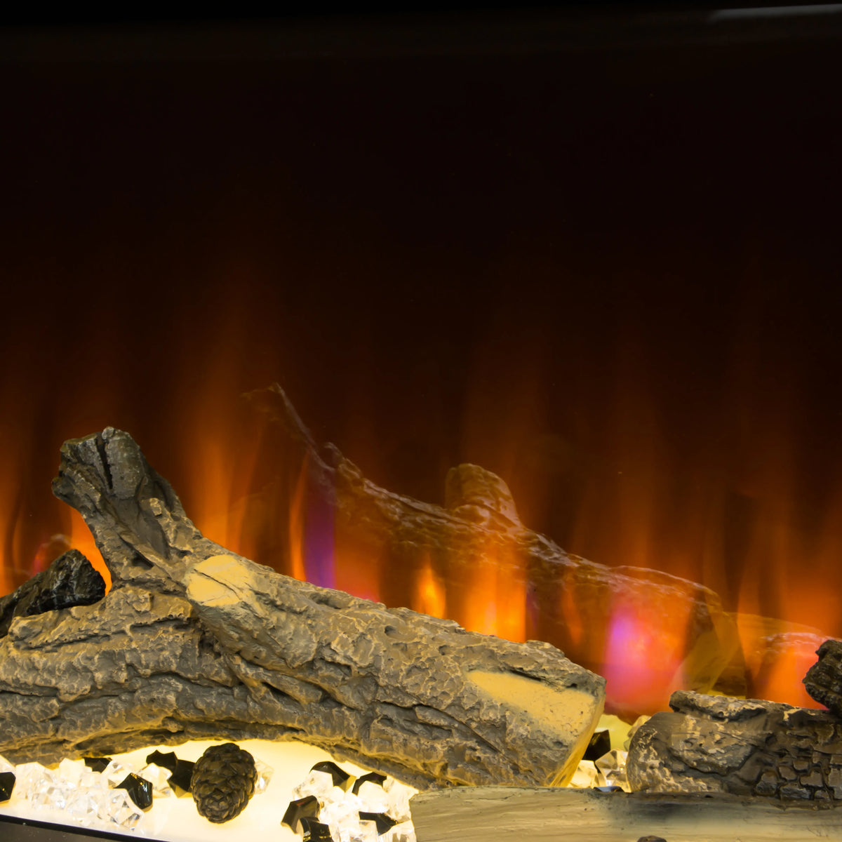 Close-up of a fireplace or electric fireplace showing faux logs, glowing orange and yellow flames, and colorful flame effects against a dark background.