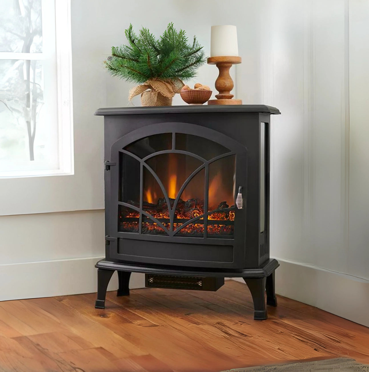 Black electric stove with glowing interior, decorative items on top, in a room with wooden floor and window.